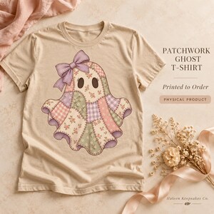 May include: A beige t-shirt featuring a graphic of a ghost made of patchwork fabric patterns in shades of pink, purple, and green. The ghost has a large purple bow on its head and dark oval eyes. Text on the shirt reads PATCHWORK GHOST T-SHIRT.