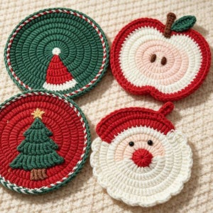 Puede incluir: Cuatro posavasos de ganchillo con diseños festivos. Uno es verde oscuro con un gorro rojo y blanco, uno es una rodaja de manzana roja con tallo marrón y hoja verde, uno es rojo con un árbol de Navidad verde y uno es una cara de Papá Noel.