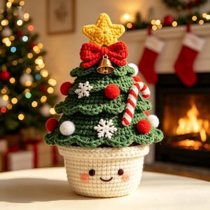 Puede incluir: Una decoración de árbol de Navidad de ganchillo en una maceta color crema con una cara sonriente. El árbol verde presenta una estrella amarilla, un lazo rojo con una campana dorada, copos de nieve blancos, pompones rojos y blancos y un bastón.