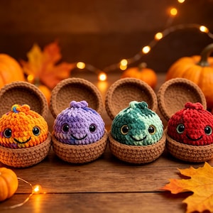 Puede incluir: Cuatro pequeñas criaturas de peluche tejidas a ganchillo en naranja, morado, verde azulado y rojo, cada una dentro de una cáscara marrón tejida con forma de bellota. Cada criatura tiene grandes ojos negros y una sonrisa cosida simple.