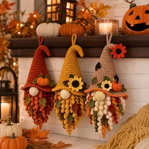 Puede incluir: Tres adornos colgantes de gnomos tejidos a ganchillo con gorros puntiagudos en naranja quemado, amarillo mostaza y beige. Cada gnomo tiene una barba texturizada de pequeños bucles, decorada con calabazas, girasoles y hojas de otoño.