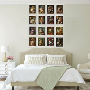 May include: A white bedroom with a bed, a chair, and a wall gallery of 16 framed floral still life paintings. The bed has a white duvet and a green throw blanket. The chair has a white cushion and a beige throw pillow. The wall gallery is arranged in a grid pattern.
