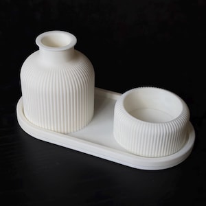Peut inclure: Un ensemble blanc composé d'un plateau ovale, d'un vase cannelé et d'un bol cannelé assorti. Le vase présente un col étroit et un corps large, tandis que le bol est court et cylindrique. Les trois pièces ont une texture nervurée verticale.