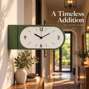Puede incluir: Un reloj de pared ovalado con un marco verde oliva mate y una esfera blanca. El reloj cuenta con manecillas negras para las horas y los minutos, con los números 12, 3, 6 y 9 impresos en verde. El texto A Timeless Addition TO YOUR HOME es visible.