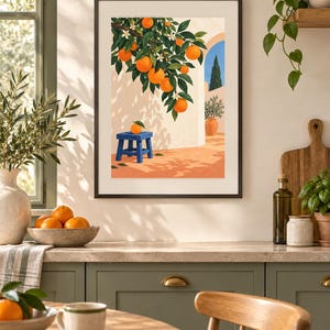 May include: A framed wall art print depicting a Mediterranean scene with an orange tree branch laden with ripe fruit and white blossoms hanging over a small blue wooden stool. The background shows a sunlit patio with a terracotta floor and archway.