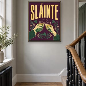 Pu&ograve; includere: Una stampa artistica da parete rettangolare con sfondo viola scuro e la parola SL&Aacute;INTE in grandi lettere dorate. Sotto il testo, due mani sono raffigurate mentre brindano con bicchieri pieni di un liquido dorato, circondate da trifogli verdi.