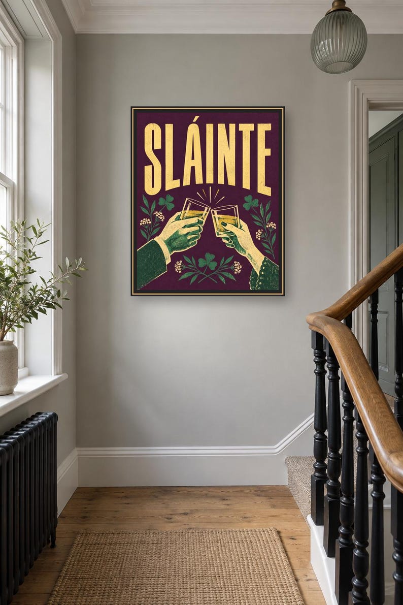 Pu&ograve; includere: Una stampa artistica da parete rettangolare con sfondo viola scuro e la parola SL&Aacute;INTE in grandi lettere dorate. Sotto il testo, due mani sono raffigurate mentre brindano con bicchieri pieni di un liquido dorato, circondate da trifogli verdi.