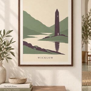 Peut inclure: Une affiche encadr&eacute;e repr&eacute;sentant une illustration de paysage stylis&eacute;e avec une haute tour violet fonc&eacute; situ&eacute;e pr&egrave;s d'une rivi&egrave;re, entour&eacute;e de collines vertes. Le mot WICKLOW est imprim&eacute; en lettres capitales noires au bas de l'affiche cr&egrave;me.