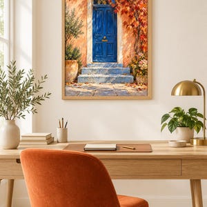 May include: A framed wall art print depicting a vibrant blue door set into a peach-coloured wall, surrounded by autumn foliage in shades of red and orange. The scene includes stone steps leading to the entrance and potted plants on either side.