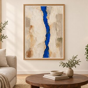 May include: A framed abstract painting featuring a vertical, jagged strip of vibrant cobalt blue running through the center, flanked by textured, layered sections of cream, beige, tan, and light gray tones with a visible impasto paint application.