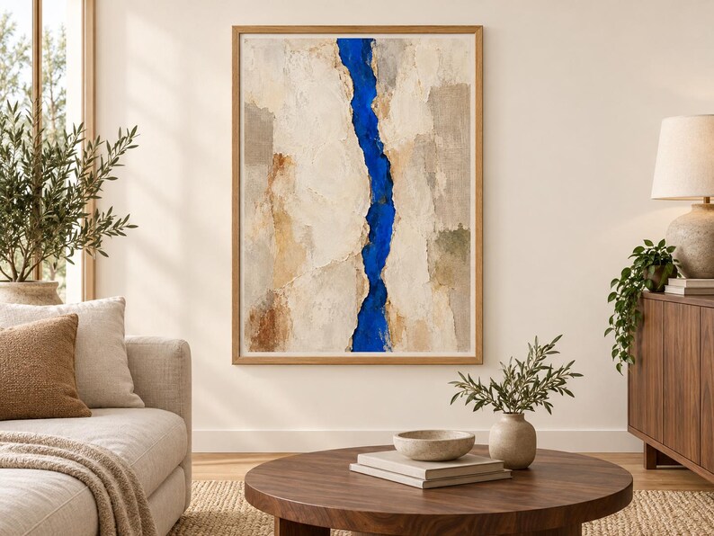 May include: A framed abstract painting featuring a vertical, jagged strip of vibrant cobalt blue running through the center, flanked by textured, layered sections of cream, beige, tan, and light gray tones with a visible impasto paint application.