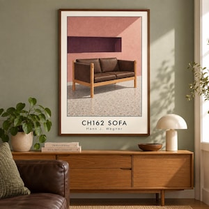 Op de afbeelding: Een ingelijste wandkunstprint met een bruine leren bank met een lichthouten frame, tegen een roze en paarse muur. De tekst CH162 SOFA Hans J. Wegner staat in het zwart gedrukt onderaan de poster met witte rand.