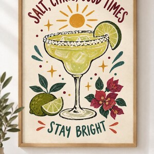 May include: A framed wall art print featuring a margarita in a glass with a salted rim, ice cubes, and a lime wedge. The text reads SALT, CITRUS, GOOD TIMES and STAY BRIGHT. The illustration includes a yellow sun, lime fruit, and red flowers.