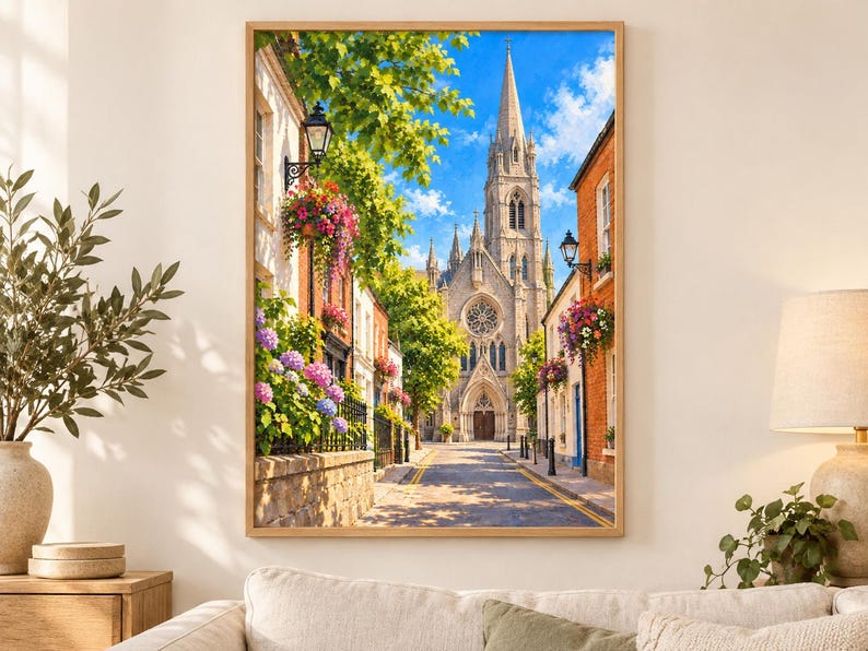 Pu&ograve; includere: Una stampa d'arte da parete incorniciata che raffigura una stretta strada europea che conduce a un'alta chiesa in pietra con una guglia. La scena presenta edifici in mattoni, cesti di fiori appesi con fiori rosa e viola, alberi verdi e un cielo blu.