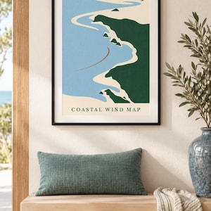 May include: A framed wall art print titled COASTAL WIND MAP featuring a stylized illustration of a coastline with dark green land, light blue water, and a thin red curved line. The print is displayed in a thin black frame on a neutral wall.