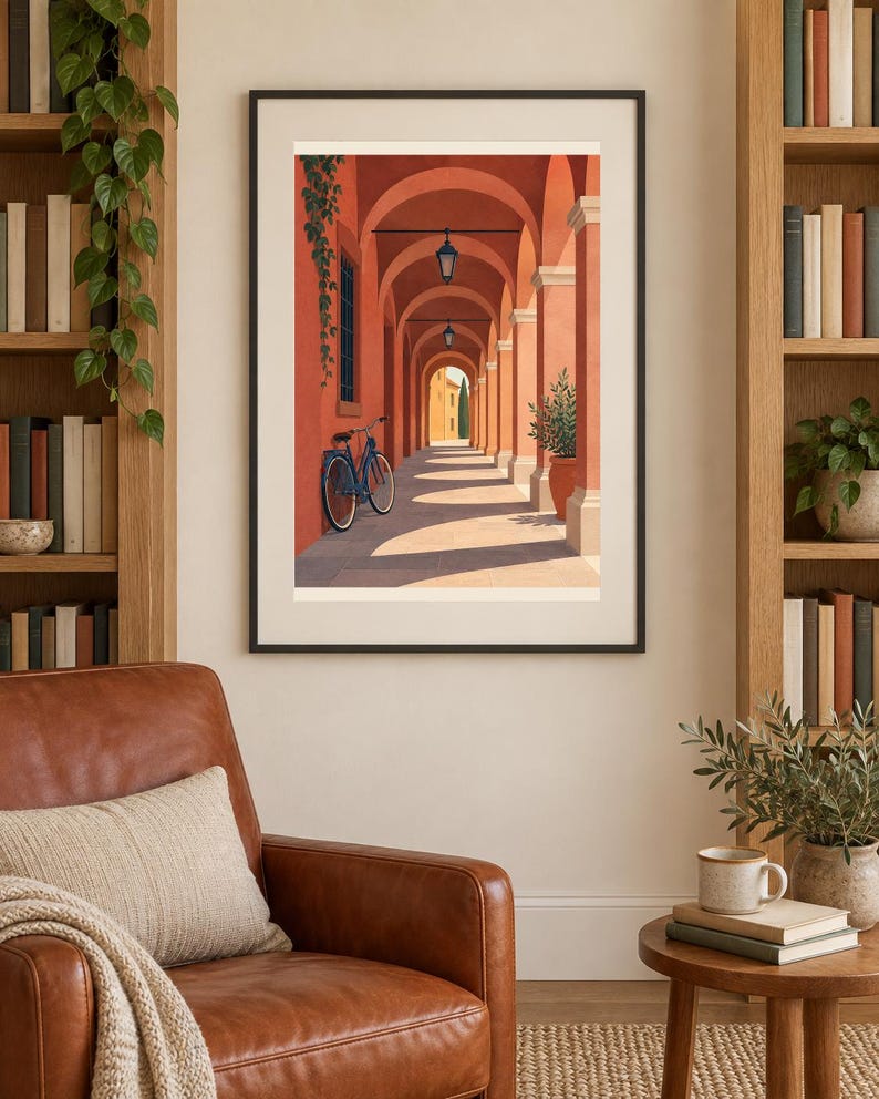 Pu&ograve; includere: Una stampa artistica incorniciata che raffigura un porticato color terracotta illuminato dal sole con una bicicletta blu appoggiata a una colonna. La scena presenta lanterne sospese, una pianta in vaso e un edificio in lontananza.