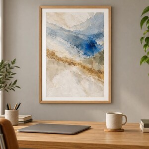 Puede incluir: Una l&aacute;mina de arte mural abstracto enmarcada con capas texturizadas en tonos crema, beige y marr&oacute;n, contrastadas por una mancha central de color azul intenso. La obra est&aacute; contenida en un marco de madera clara con una composici&oacute;n fluida.