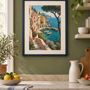 May include: A framed art print featuring a coastal Mediterranean scene with colourful buildings, stone stairs, and small boats floating in a turquoise bay. The artwork is enclosed in a dark blue frame with a cream-coloured mat, displayed on a wall.