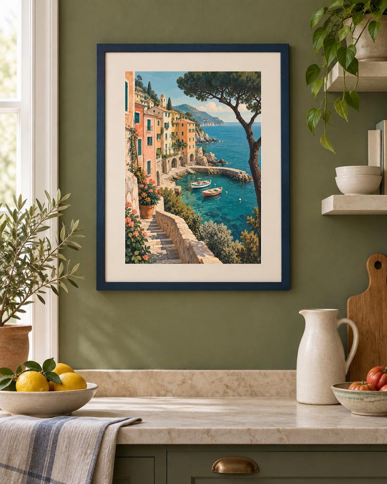 May include: A framed art print featuring a coastal Mediterranean scene with colourful buildings, stone stairs, and small boats floating in a turquoise bay. The artwork is enclosed in a dark blue frame with a cream-coloured mat, displayed on a wall.