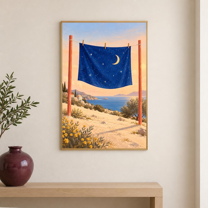 May include: A framed wall art print depicting a dark blue fabric sheet with a crescent moon and stars hanging on a clothesline between two red wooden posts, set against a coastal landscape with yellow flowers, hills, and a blue sea.
