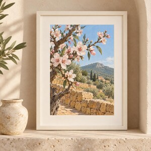 May include: A framed wall art print featuring a landscape painting of a blooming almond tree with light pink flowers in the foreground, set against a stone terrace, olive trees, and a distant mountain under a clear blue sky.