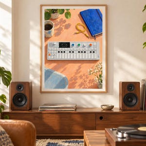 Pu&ograve; includere: Una stampa artistica incorniciata che mostra una vista dall'alto di un sintetizzatore bianco Teenage Engineering OP-1, un taccuino blu, un cavo audio giallo, una tazza di caff&egrave; e piccoli fiori bianchi su una superficie arancione, appesa tra due casse.