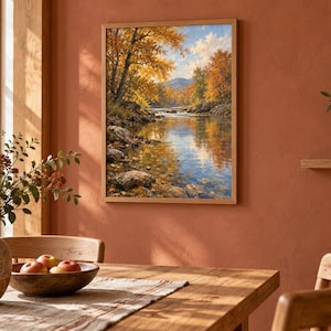 K&ouml;nnte beinhalten: Ein gerahmter Wandkunstdruck, der eine Landschaft mit einem flie&szlig;enden Fluss, felsigen Ufern und B&auml;umen mit leuchtend gelbem und orangefarbenem Herbstlaub unter einem hellen Himmel mit Bergen im Hintergrund zeigt.