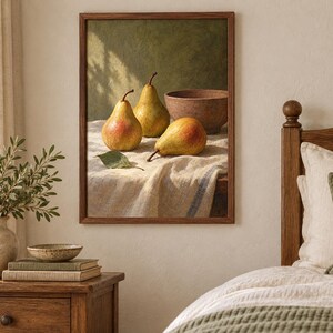May include: A framed wall art print depicting a still life scene with three yellow and red pears and a brown bowl resting on a textured white cloth. The painting features a dark green background and is displayed in a simple wooden frame.
