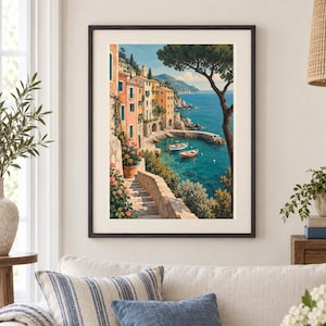 May include: A framed wall art print depicting a coastal Mediterranean village with pastel-coloured buildings, a stone staircase leading down to the turquoise sea, two small boats floating in the water, and a large tree framing the right side.