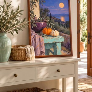 May include: A framed wall art print depicting a Mediterranean landscape at twilight with a full moon over the sea. The scene features a weathered turquoise table holding a purple bowl, olive branches, and two pumpkins, with a lavender cloth draped nearby.