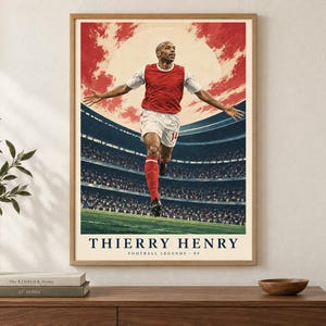 Może przedstawiać: Oprawiony plakat przedstawiający piłkarza w czerwono-białym stroju z rozłożonymi ramionami na tle stadionu i czerwonego nieba. Tekst na dole brzmi THIERRY HENRY oraz FOOTBALL LEGENDS 09 i jest napisany ciemnoniebieską czcionką.