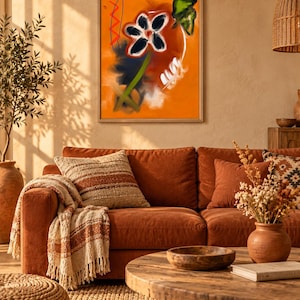 May include: A framed wall art print featuring an abstract orange background with a central dark flower, a green stem, a red zigzag line, and white brushstroke accents. The artwork is displayed in a light-colored wooden frame on a wall.