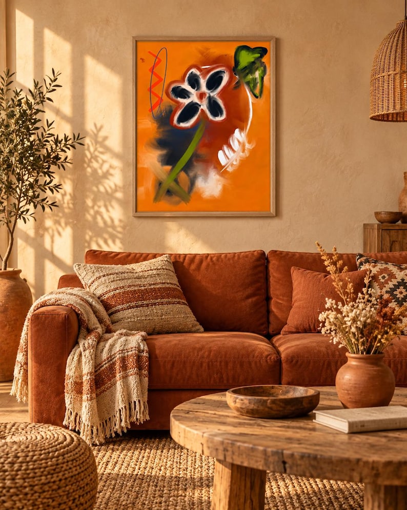 May include: A framed wall art print featuring an abstract orange background with a central dark flower, a green stem, a red zigzag line, and white brushstroke accents. The artwork is displayed in a light-colored wooden frame on a wall.