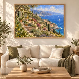 Puede incluir: Un cuadro de paisaje enmarcado que representa una escena costera mediterr&aacute;nea con una terraza de piedra, limoneros, arbustos en flor y una vista del mar azul con veleros. La obra de arte se exhibe en una pared sobre un sof&aacute; de color beige.