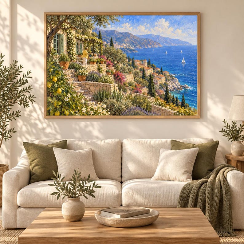 Puede incluir: Un cuadro de paisaje enmarcado que representa una escena costera mediterr&aacute;nea con una terraza de piedra, limoneros, arbustos en flor y una vista del mar azul con veleros. La obra de arte se exhibe en una pared sobre un sof&aacute; de color beige.