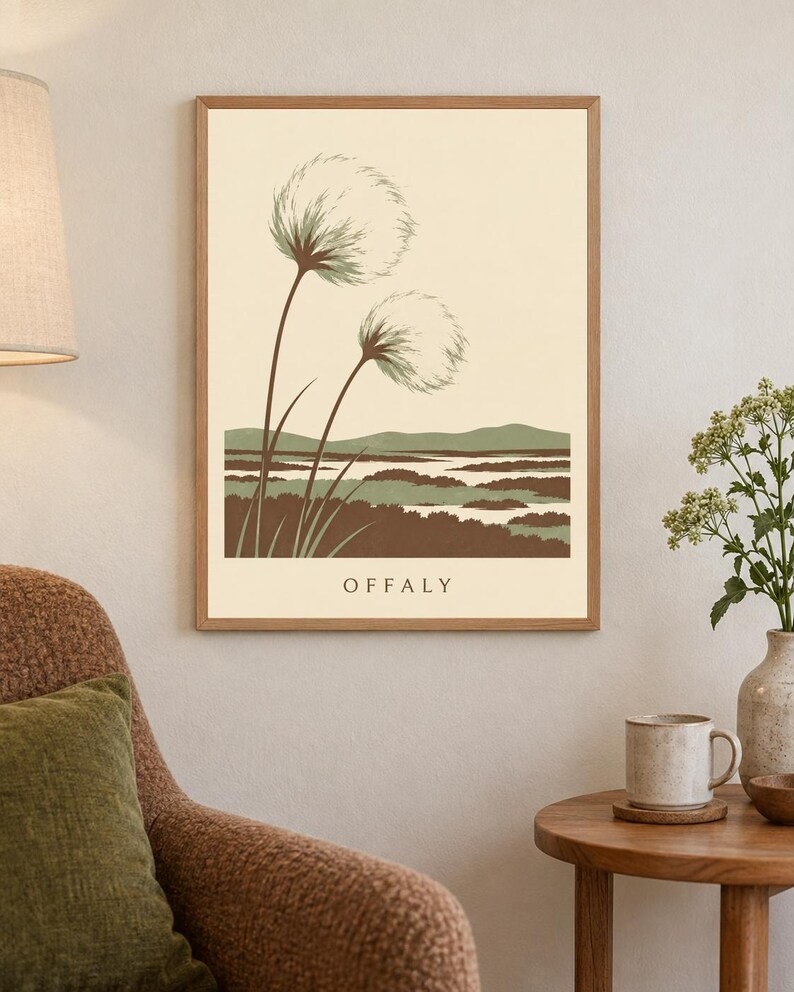 May include: A framed rectangular wall art print featuring a cream background with two stylized fluffy seed heads on long stems. Below the plants is a landscape of brown and green hills and water. The word OFFALY is printed in black at the bottom.