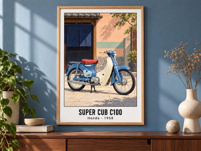 May include: A framed wall print featuring a blue Honda Super Cub C100 motorcycle with a red seat and cream-colored leg shield, parked in front of a building with a blue curtain. The text SUPER CUB C100 Honda 1958 is printed at the bottom.