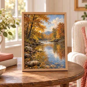 K&ouml;nnte beinhalten: Ein gerahmtes Landschaftsgem&auml;lde, das einen Fluss zeigt, der im Herbst durch einen Wald flie&szlig;t. Die Szene umfasst goldene und orangefarbene B&auml;ume, felsige Ufer und ferne Berge unter einem blauen Himmel, eingefasst in einen hellen Holzrahmen.