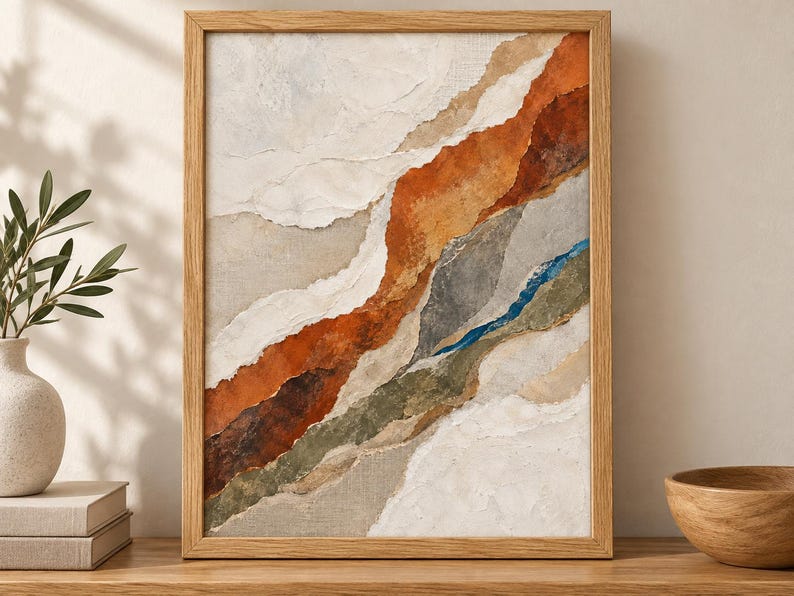 May include: A framed abstract wall art piece featuring layered, torn-paper style textures in shades of burnt orange, cream, sage green, gray, and a thin streak of deep blue. The artwork is encased in a light-toned wooden frame with a clean finish.
