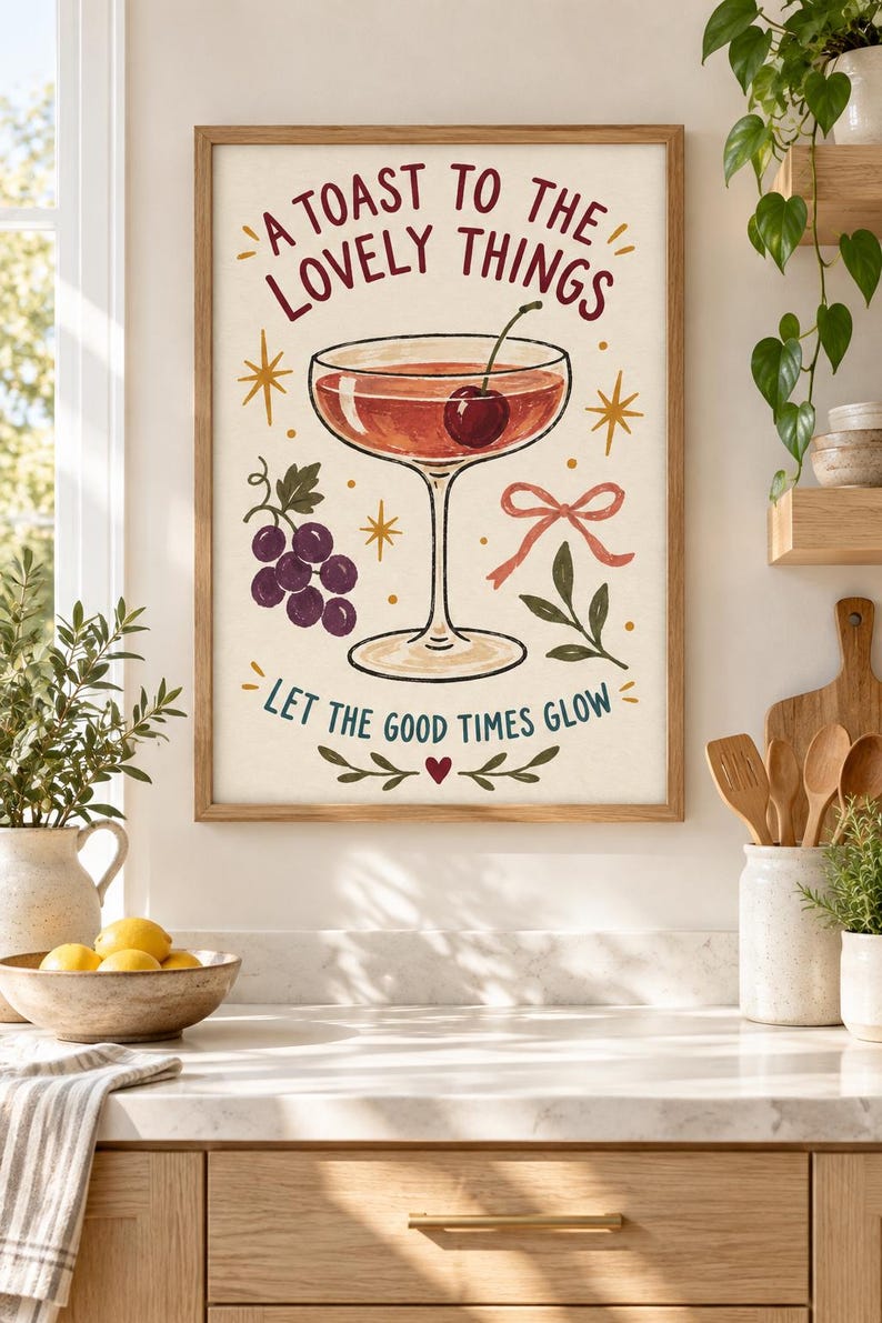 May include: A framed wall art print featuring a cocktail glass with a cherry, a cluster of purple grapes, a pink ribbon, and gold star accents. The text reads A TOAST TO THE LOVELY THINGS and LET THE GOOD TIMES GLOW, with a small red heart at the bottom.