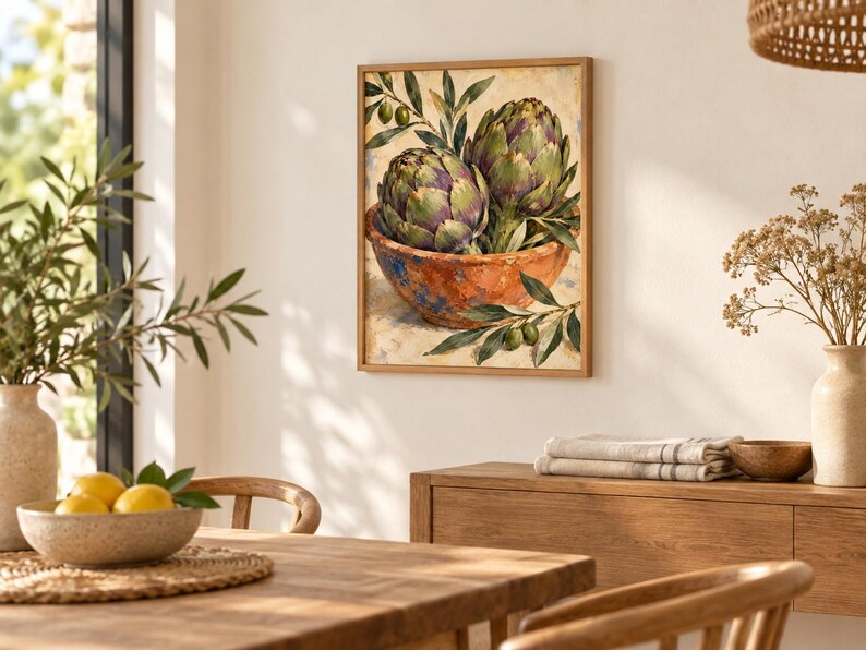 May include: A framed wall art print featuring an oil painting of two green artichokes resting in a rustic, textured terracotta-colored bowl, accented with small green olive branches and leaves against a neutral, light-colored background.