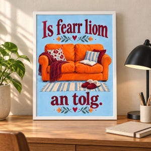 K&ouml;nnte beinhalten: Ein gerahmter Druck mit einem orangefarbenen Sofa auf blauem Hintergrund und dem Text Is fearr liom an tolg. Das Sofa hat eine kastanienbraune Decke, ein Blumenkissen, ein blau-wei&szlig; gestreiftes Kissen, ein offenes Buch und rote Hausschuhe auf einem Teppich.