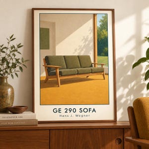 May include: A framed art print featuring a three-seat sofa with olive green cushions and a light wood frame. The illustration depicts the furniture in a sunlit room with a yellow floor and outdoor greenery. The text reads GE 290 SOFA Hans J. Wegner.