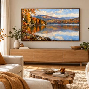 Pode incluir: Uma televis&atilde;o retangular montada na parede exibindo uma pintura de paisagem de um lago cercado por &aacute;rvores de outono com folhagem laranja e amarela, contra um fundo de montanhas azuis distantes sob um c&eacute;u brilhante com nuvens brancas.