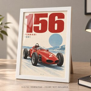 May include: A framed print featuring a red 1961 Ferrari 156 race car with the number 2 on its side. The artwork displays the text 156, FERRARI, and 1961 against a light background with a blue circular shape and a landscape illustration below the car.