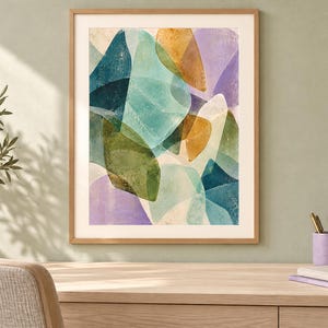 May include: A framed wall art print featuring an abstract composition of overlapping organic shapes in shades of teal, olive green, mustard yellow, and soft lavender. The artwork is enclosed in a light-toned wooden frame with a white mat border.