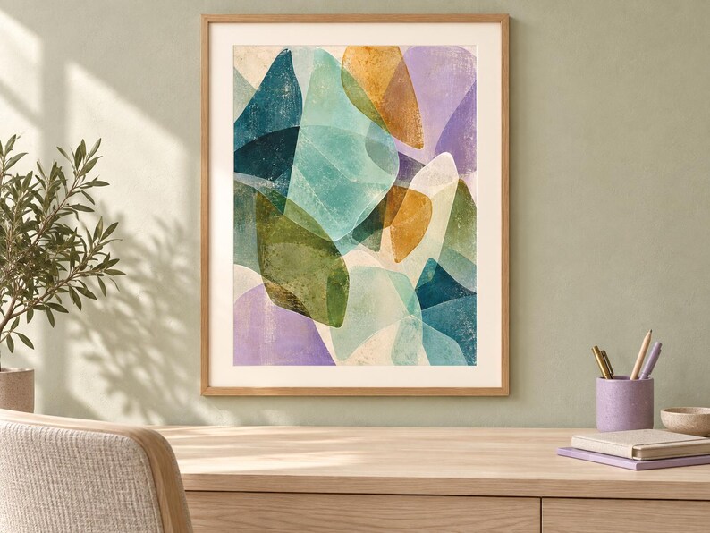 May include: A framed wall art print featuring an abstract composition of overlapping organic shapes in shades of teal, olive green, mustard yellow, and soft lavender. The artwork is enclosed in a light-toned wooden frame with a white mat border.