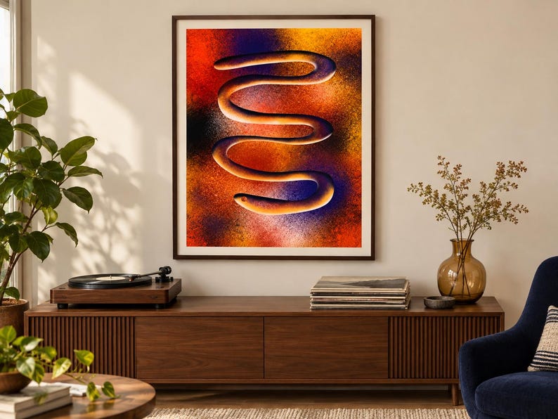 Puede incluir: Una impresi&oacute;n de arte mural enmarcada que presenta una forma serpentina horizontal central con una superficie lisa y clara. El fondo es un degradado texturizado y vibrante de rojo, naranja, amarillo y morado intenso, creando un efecto visual.