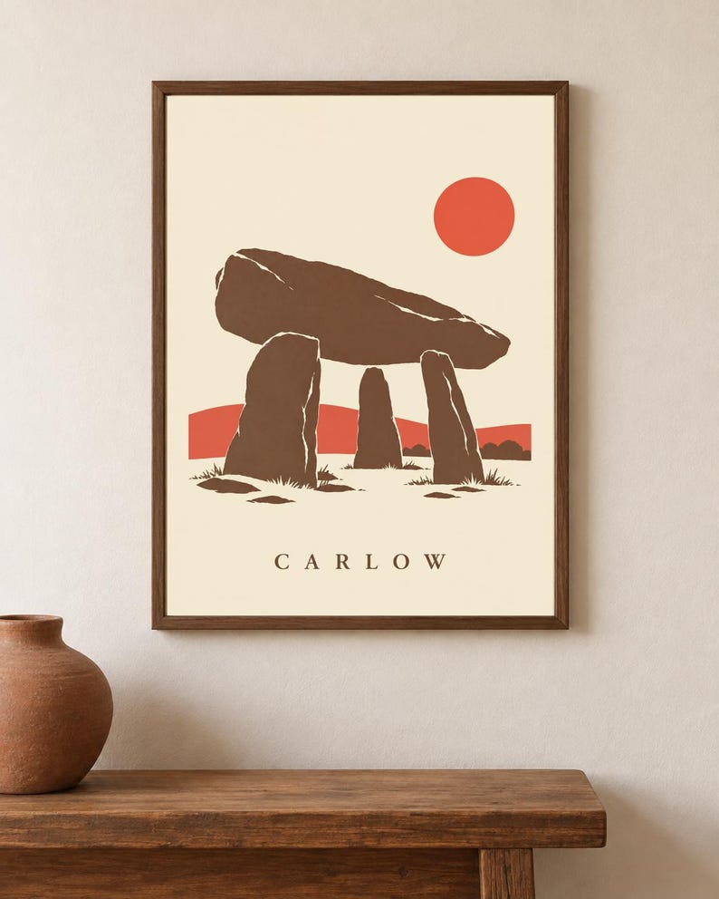 May include: A framed wall art print featuring a brown megalithic dolmen structure against a cream background. The design includes a solid red sun, red hills, and the text CARLOW printed in brown at the bottom center of the rectangular composition.