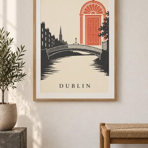 K&ouml;nnte beinhalten: Ein gerahmter Kunstdruck mit einer stilisierten Illustration von Dublin. Die Grafik zeigt die dunkle Silhouette von Geb&auml;uden und einer Br&uuml;cke &uuml;ber einen Fluss, mit einer markanten orangefarbenen Bogent&uuml;r im Hintergrund. Das Wort DUBLIN steht unten.